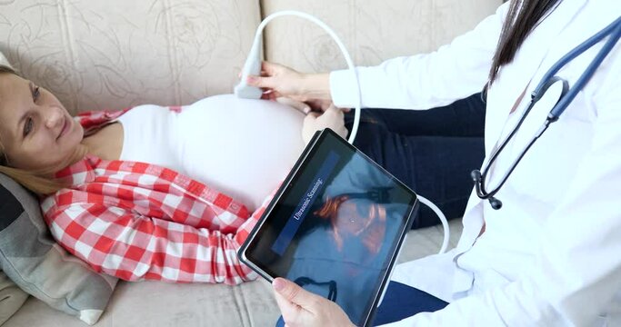Doctor makes ultrasound sonogram of pregnant woman at home closeup