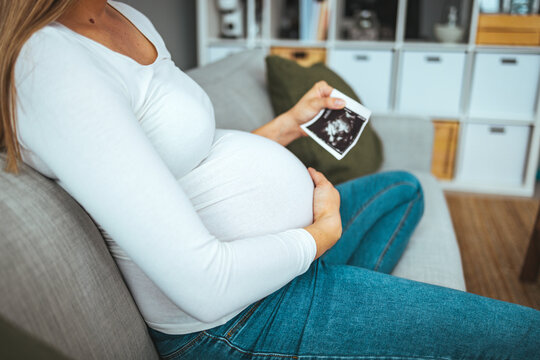 Pregnant woman holding ultrasound image. Concept of pregnancy, health care, gynecology, medicine. Young mother waiting of the baby. Close-up, copy space, indoors.