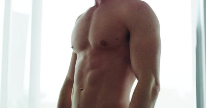 Abs that speak for themselves. Close up of a muscular man standing shirtless and posing with his fit body. Young man rubbing his hands together and showing off his six pack