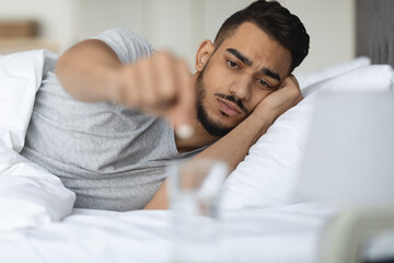 Fototapeta na wymiar Sick Arab Guy Putting Pill Into Water Glass While Lying In Bed