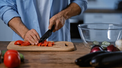 cropped view of man cutting tomatoes near blurred eggplants and glass bowl.