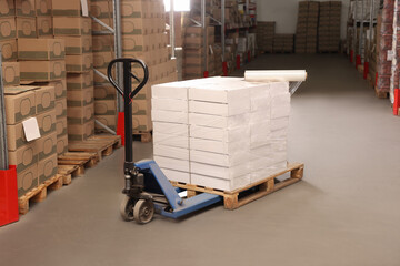 Manual pallet truck with stacked boxes and roll of stretch wrap in warehouse