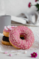 Sweet pink donut close up with white sprinkles and tea cup on a white background. Sweet breakfast concept.