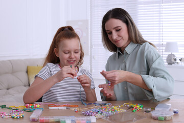 Happy mother with her daughter making beaded jewelry at home
