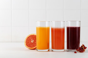 Three Freshly squeezed juices in glass on white table. Red orange, grapefruit, pomegranate juice for menu. Mock up
