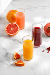 Three Freshly squeezed juices in glass on white table. Red orange, grapefruit, pomegranate juice...
