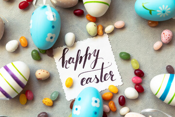 Fototapeta na wymiar Happy Easter concept. Preparation for holiday. Easter eggs Inscription HAPPY EASTER letters candy chocolate eggs and jellybean sweets on concrete stone grey background. Flat lay top view copy space