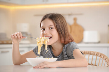 Happy girl eating tasty pasta at table in kitchen
