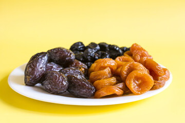 Dried apricots, prunes and dates dried fruits on a light plate close-up.