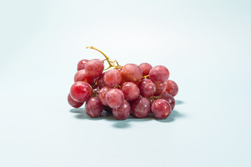 A branch of grapes with red berries on a light blue background close-up.