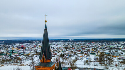 Aerial view of a Catholic cross on the spire of a Gothic cathedral. In the background is a small town in winter.