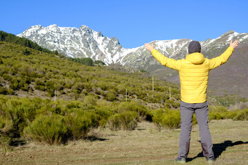 a man raises his arms near the snow-capped mountains. Enjoying nature alone