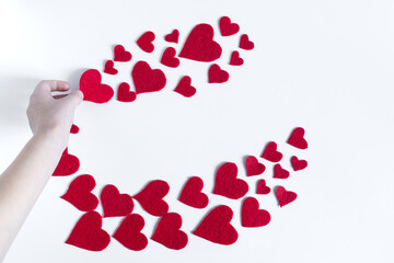 The hand lays out a red heart on a white background with large and small red hearts on a light background top view.