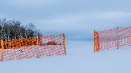 Orange perforated plastic foil barriers against snow in farmland. This protects the snow cover on...