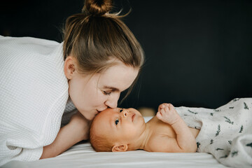 Mother kissing one month old baby on forehead, lying in bed.
