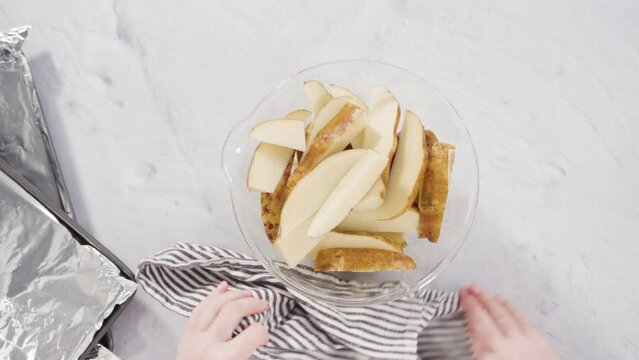 Time lapse. Flat lay. Step by step. Preparing russet potatoes in wedges with olive oil and spices to bake in the oven.