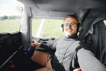 Selfie photo happy man pilot in light aircraft cockpit, aviator headset and steering wheel © Parilov