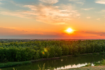 The heavenly light of the sun over the river and the forest.Dramatic evening sky with clouds and rays of the sun.Golden hour at evening sunset or morning sunrise.Panoramic view of cirrus clouds