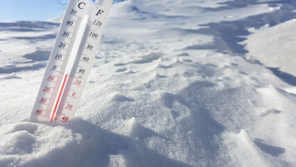 The thermometer lies on the snow and shows a negative temperature in cold weather on the blue sky.Meteorological conditions with low air and ambient temperatures.Climate change and global warming