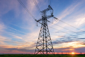 high voltage power lines in the field against the backdrop of a bright and colorful sunset or dawn