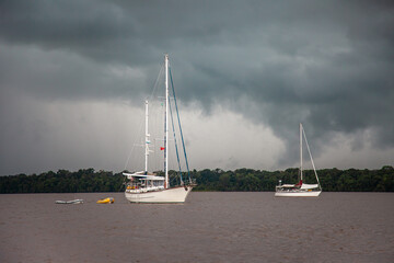 Yachts standing on the river on a clear sunny day against the background of green trees and dark storm clouds, Guyana. Travel adventure ships, subtropics.