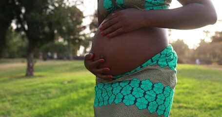 Young african pregnant woman having tender moment touching her belly at city park