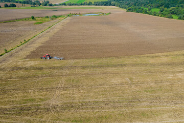 A red tractor plows the land on a plantation. View from above.