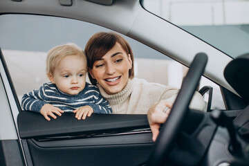 Woman with baby son choosing a car in a car salon
