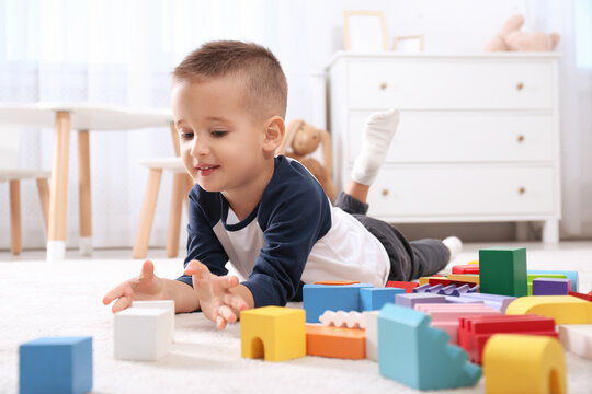 Cute little boy playing with colorful building blocks on floor in room