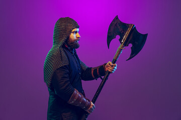 Studio shot of young bearded man in image of medieval warrior, archery in chain armor with ax...