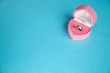 Jewelry engagement ring made of gold in pink box in shape of heart on flat beautiful blue background. Concept of gift, joy, happiness, family, love, valentine's day