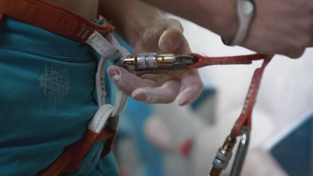 A sporty man fastens the belay with a carabiner on his body. Ready to climb the bouldering wall. Caucasian man attaching carabiner to safety harness, climbing up artificial indoor wall. Slow motion
