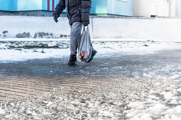 People walk on a slippery road made of melted ice. View of the legs of a man walking on an icy...