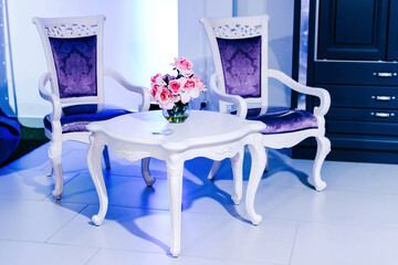 Composition of designer white furniture and a bouquet of flowers in lilac light