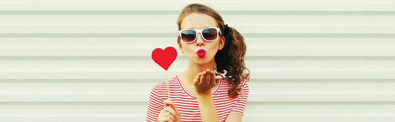 Portrait of beautiful young woman blowing her lips with lipstick with red sweet heart shaped...