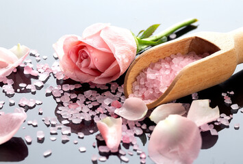 Spa and bath interior concept. Pink roses petals and wooden spoon on a salt on the black background