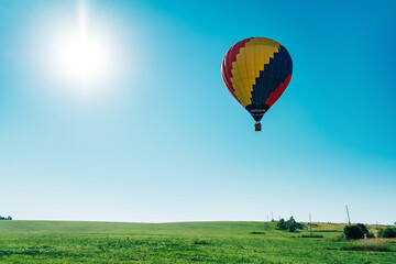 Multicolored hot air balloon on blue sky over village field