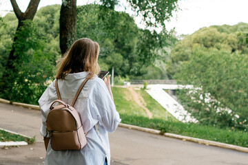 Girl in a white shirt with a phone from behind in a summer park