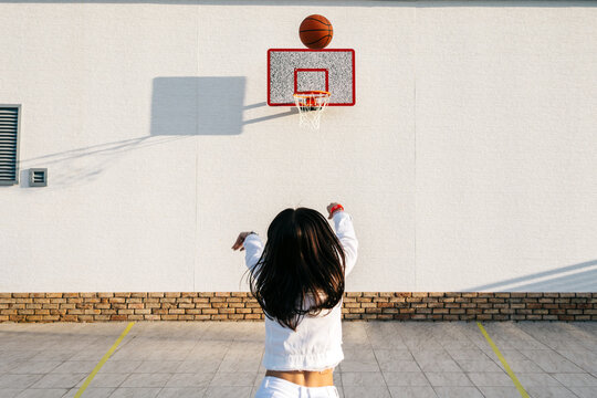 Girl from behind throws a basketball into the basket on the street