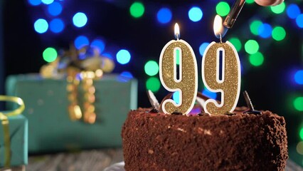 Birthday candle number ninety nine on a sweet cake on the table, 99th birthday. Fire from the lighter, blow out the holiday candle.