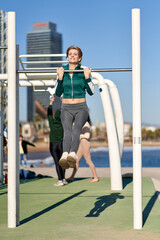 Obraz premium athletic fitness woman working out at outdoor gym doing pull ups