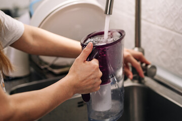 Woman pouring water from faucet into water filter jug at the kitchen. Healthy lifestyle. Woman filling water