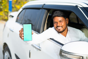 Foucs on mobile, cab driver showing mobile phone with green screen mockup by looking at camera -...