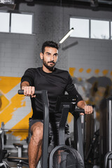 Fototapeta na wymiar Muslim sportsman training on elliptical trainer in blurred gym.