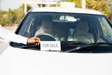 Close up shot of owner placing car for sale sign board in front of car - concept of business loss,...