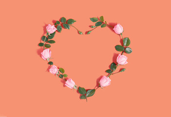 Creative love concept with pink roses and green leaves. Minimal idea of the heart on tawny orange background. Flet lay. © Suzana