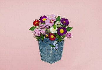 Blooming summer flowers in a jeans pocket against pastel pink background. Minimal creative idea flat lay.