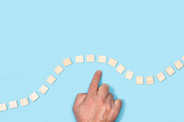 Elegir a mano un bloque de madera de un conjunto sobre un fondo celeste liso y aislado. Vista superior. Copy space. Concepto de elecci&oacute;n de negocio 