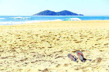 Fototapeta na wymiar Flip Flop On Paradise. A pair of red sandals on beach sand, Praia do Campeche with an island at horizon on Florianópolis Southern Brazil 