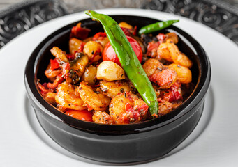 Shrimp stew with tomatoes, garlic and peppers in a black stone bowl